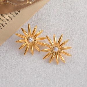 Elegant gold sunflower earrings with white pearl center on a minimalist textured background
