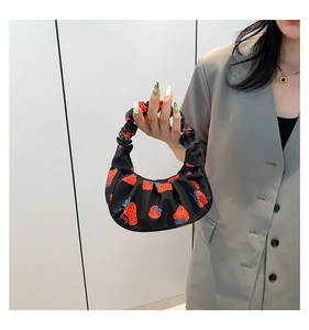Dettaglio di una borsa a tracolla nera con stampa a fragole e design a nuvola pieghettata