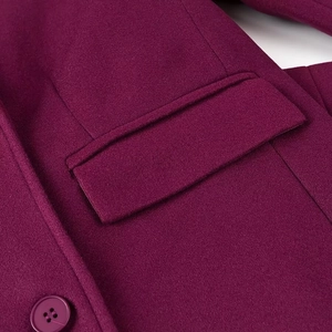 Détail de la texture en laine avec poche à rabat et bouton rond sur un manteau prune