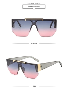 Dettaglio occhiali da sole oversize con lenti sfumate grigio-rosa e barra in metallo oro