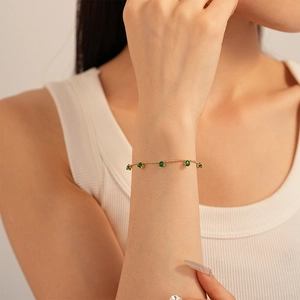 Detail of elegant gold chain bracelet featuring five vibrant green round-cut gemstones