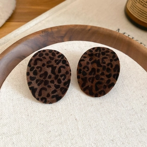 Close-up of oval leopard print earrings with flocked texture on rustic linen padding