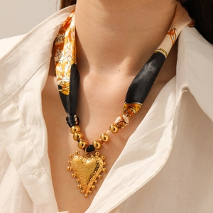 Detail of a vintage gold heart pendant on a printed black and orange silk ribbon necklace