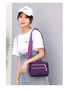 Detail of purple nylon crossbody bag featuring three golden zipper front pockets and strap