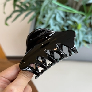 Détail d'une pince à cheveux noire brillante montrant le ressort et la forme de requin