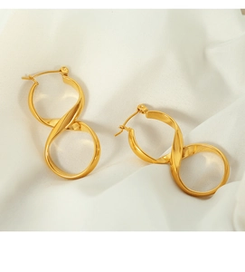Macro detail of gold wavy curved twist earrings on elegant white silk background