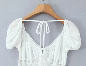 Detail showing the white backless dress with elegant tie-back design and ruched waist