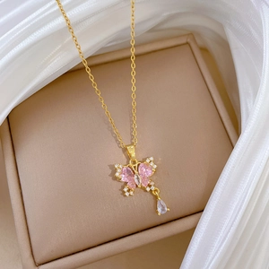Dettaglio collana dorata con ciondolo a farfalla rosa e goccia di cristallo scintillante