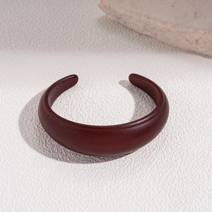 Close-up of deep brown C-shaped open bangle with smooth matte finish on a minimalist stone base