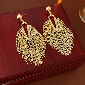 Detail of golden tassel earrings with fine metal beads on a vintage wooden jewelry box