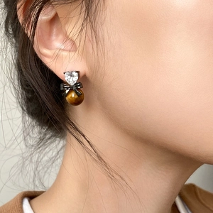 Detail of silver needle heart zircon and tiger eye stone earring on model's ear