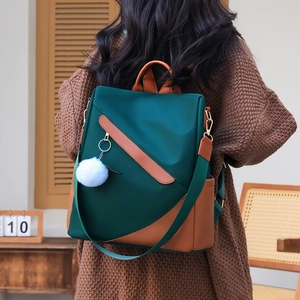 Waterproof dark green women's backpack with brown leather trim and white fluffy charm