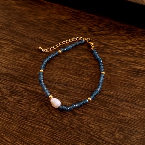 Detailed shot of faceted blue beads and irregular natural pearl on a delicate gold chain