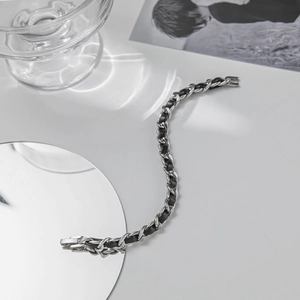 Minimalist silver steel chain bracelet woven with black leather on reflective mirror surface