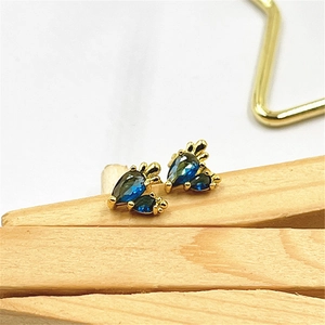 Close-up of gold stud earrings with teardrop-cut dark blue stones on a wooden block