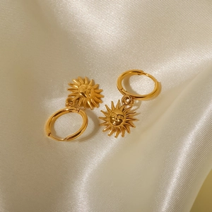 Detailed view of 18K gold plated sun pendant earrings on elegant beige silk fabric