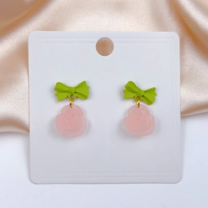 Detail view of pink frosted rose earrings with green bows on champagne silk background