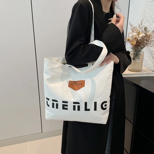 Large white canvas tote bag with black EMLIG lettering shown in a stylish urban setting