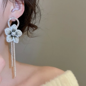 Détail de boucles d'oreilles fleurs brodées avec perle et chaînes à pompons dorés sur modèle
