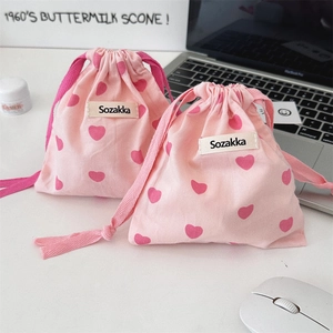 Close-up of pink drawstring canvas pouch with red heart pattern and woven label