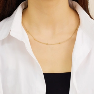 Detail of a minimalist gold layered snake chain necklace with small beads on a model