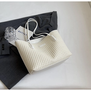 Detail of off-white woven PU leather tote bag with dual straps on fashion background