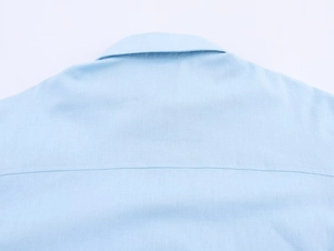 Detail shot of light blue linen shirt stitching and fabric texture on the collar and shoulder