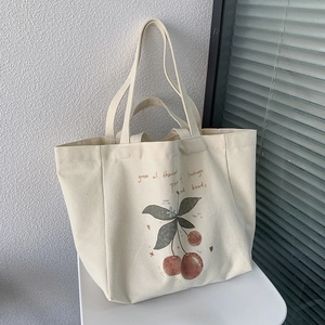 Detail of off-white canvas tote bag featuring red cherry prints and artistic lettering