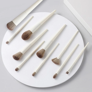 Set of 10 professional makeup brushes with beige handles arranged on a white platform