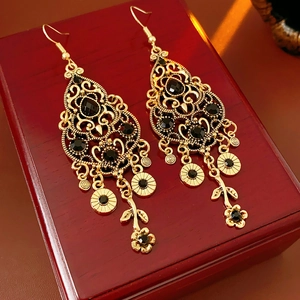 Close-up of vintage gold floral earrings with black gemstones on a red wooden base