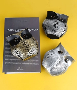 Close-up of three decorative resin owls in gold and silver finish on yellow backdrop