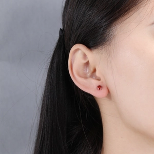 Close-up of a minimalist silver four-prong stud earring with a red round-cut zircon on ear