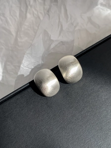 Macro detail of silver geometric stud earrings with matte brushed metal texture on black box