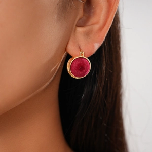 Close-up of golden geometric earrings with red velvet inlay and faux pearl accents