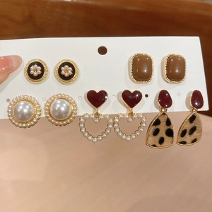 Detailed close-up of a six-pair gold earring set with pearls and resin on display card