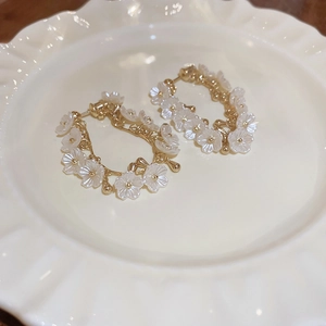Détail de boucles d'oreilles fleurs en acrylique blanc avec base dorée sur assiette