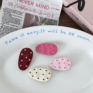 Detail of four oval polka dot hair clips in burgundy and pink on a white tray
