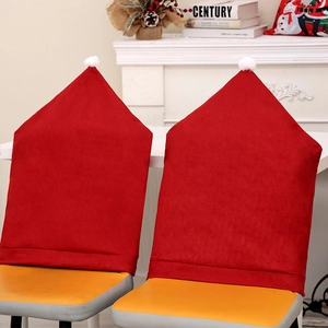 Set of 2 Red Santa Hat Christmas Chair Covers with pom-poms on chairs by a cozy fireplace