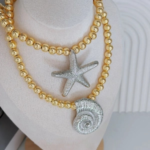 Beaded gold necklace with silver starfish and conch shell charms on jewelry display