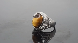 Macro shot of silver stainless steel ring with oval tiger eye stone and carved side details