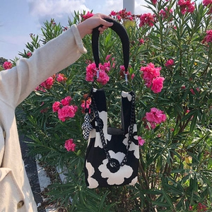 Detail of hand-held knit bag with black and white floral pattern and chain strap
