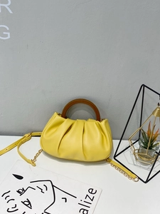 Detail of yellow pleated cloud bag featuring wooden handle and gold chain strap