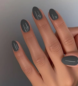 Detalle de uñas postizas almendradas gris oscuro mate en la mano con acabado de color liso