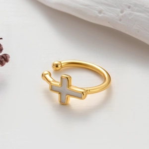 Macro shot of gold ear cuff featuring a white cross charm and delicate dried flowers
