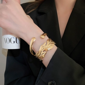 Detailed view of a gold leaf open bangle with polished metallic finish worn on wrist