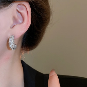 Macro shot of a sparkling C-shaped earring with paved zircons on a model ear
