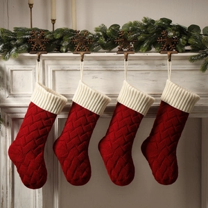 Set of 4 red knitted Christmas stockings with white cuffs hanging on a festive fireplace