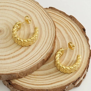 Detail of 18k gold plated C-shape twisted hoop earrings on rustic wood background