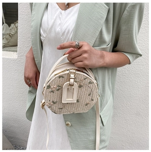 Detail of round woven straw bag with floral embroidery and white leather strap