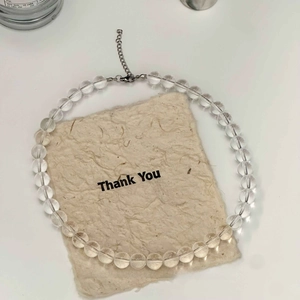 Close-up of clear round crystal glass beads necklace with silver extension chain on beige paper
